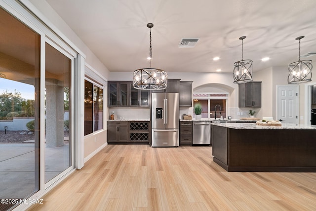 kitchen featuring appliances with stainless steel finishes, visible vents, glass insert cabinets, and dark brown cabinets