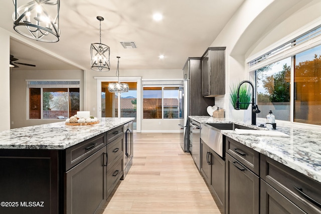 kitchen with sink, light stone counters, decorative light fixtures, light wood-type flooring, and a kitchen island