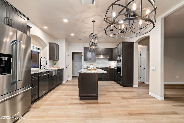 kitchen featuring a kitchen island, light stone counters, decorative light fixtures, stainless steel appliances, and under cabinet range hood