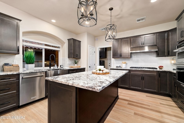 kitchen with dark brown cabinetry, under cabinet range hood, a kitchen island, hanging light fixtures, and stainless steel dishwasher