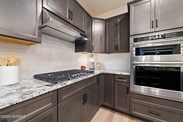 bar with tasteful backsplash, light stone countertops, light hardwood / wood-style floors, and dark brown cabinets