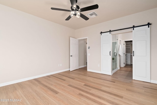 unfurnished bedroom featuring light wood-type flooring, visible vents, and a barn door