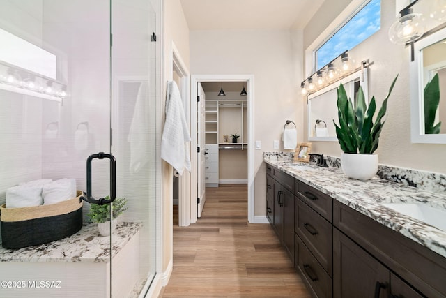 bathroom featuring double vanity, wood finished floors, a walk in closet, a shower stall, and a sink