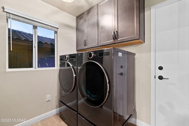 clothes washing area with cabinets, washer and dryer, and light hardwood / wood-style floors