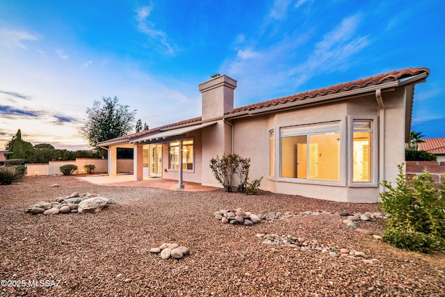 rear view of property featuring fence, a tiled roof, stucco siding, a chimney, and a patio area