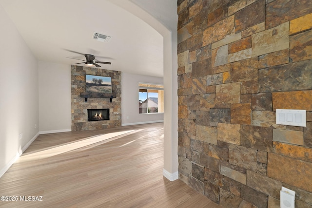 living area with arched walkways, a fireplace, visible vents, light wood-style flooring, and a ceiling fan