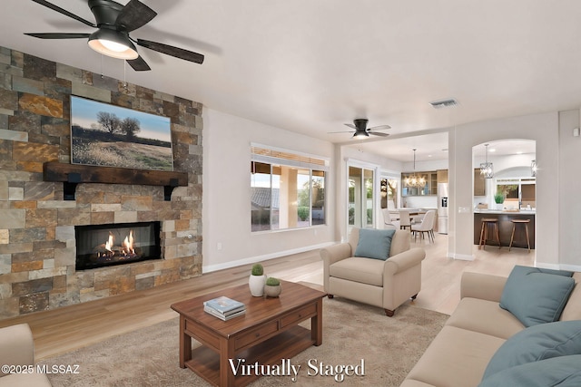 living room with ceiling fan with notable chandelier, a stone fireplace, and light hardwood / wood-style floors