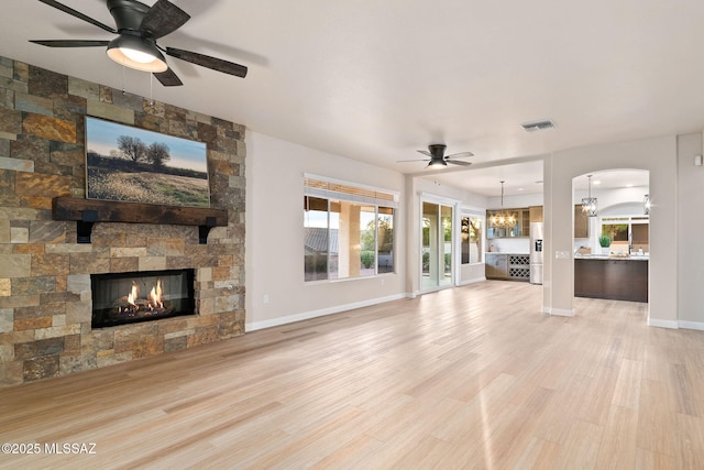 unfurnished living room with light wood-style flooring, ceiling fan with notable chandelier, a fireplace, visible vents, and baseboards