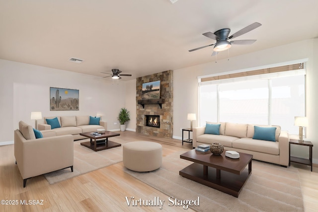 living room featuring visible vents, baseboards, light wood-style flooring, ceiling fan, and a stone fireplace