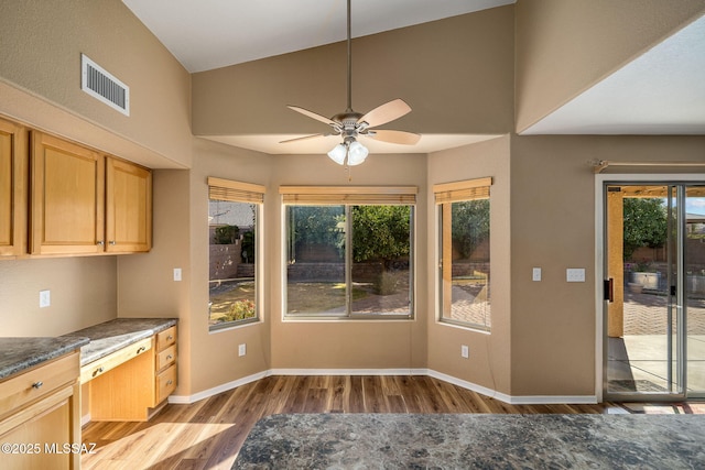 kitchen with light brown cabinetry, built in desk, light hardwood / wood-style flooring, ceiling fan, and dark stone counters