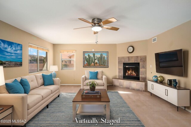 living room featuring a tiled fireplace, carpet floors, and ceiling fan