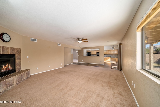 unfurnished living room with ceiling fan, light colored carpet, and a fireplace