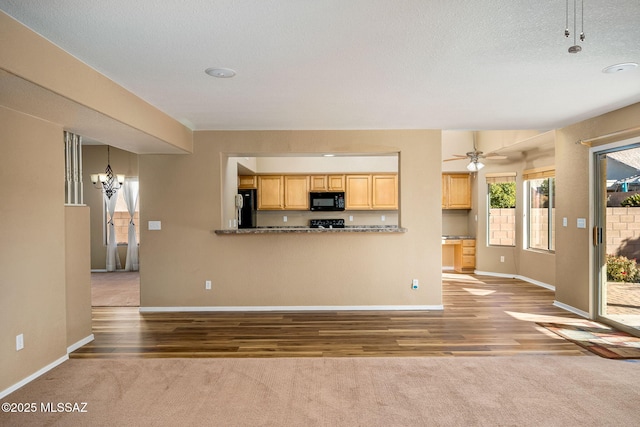 unfurnished living room featuring carpet flooring, ceiling fan with notable chandelier, and a textured ceiling