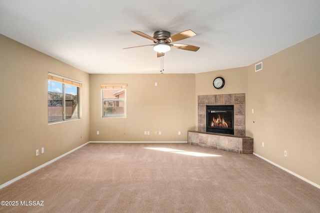 unfurnished living room featuring a tiled fireplace, carpet flooring, and ceiling fan