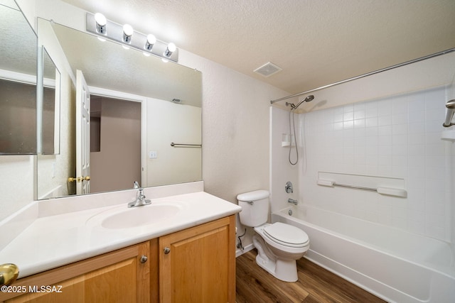 full bathroom with hardwood / wood-style flooring, tiled shower / bath combo, vanity, a textured ceiling, and toilet