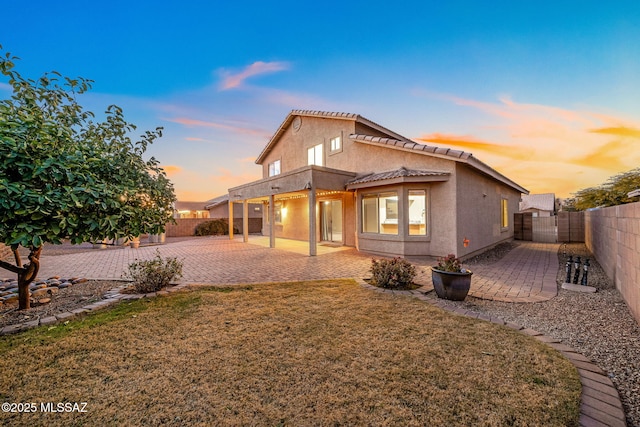 back house at dusk featuring a yard and a patio area