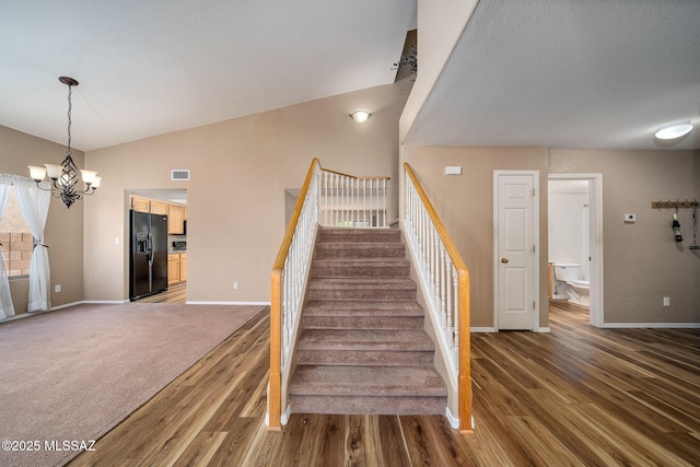 staircase with a chandelier, vaulted ceiling, and hardwood / wood-style floors