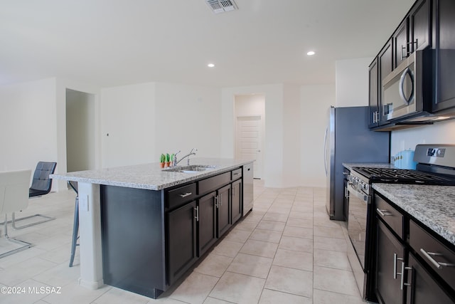 kitchen with a breakfast bar, a kitchen island with sink, light stone countertops, stainless steel appliances, and light tile patterned floors