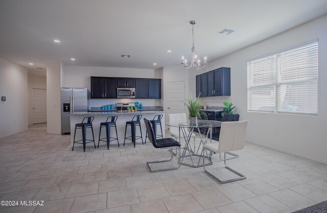 kitchen featuring a kitchen bar, a center island with sink, appliances with stainless steel finishes, decorative light fixtures, and light stone counters