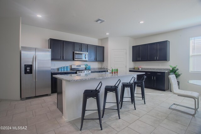 kitchen with a kitchen breakfast bar, appliances with stainless steel finishes, an island with sink, and light stone counters