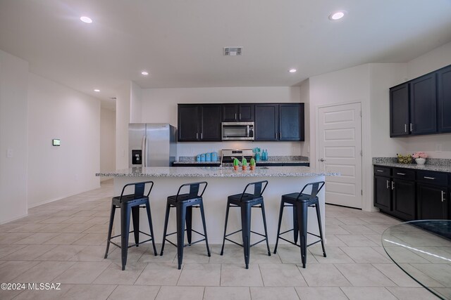 kitchen with pendant lighting, stainless steel appliances, a kitchen island with sink, a chandelier, and light stone counters