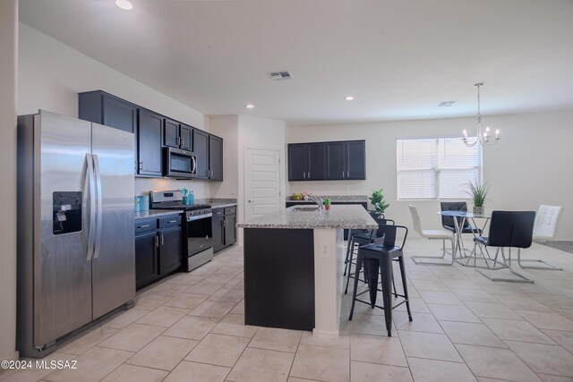 kitchen featuring a breakfast bar, appliances with stainless steel finishes, an island with sink, and light stone counters