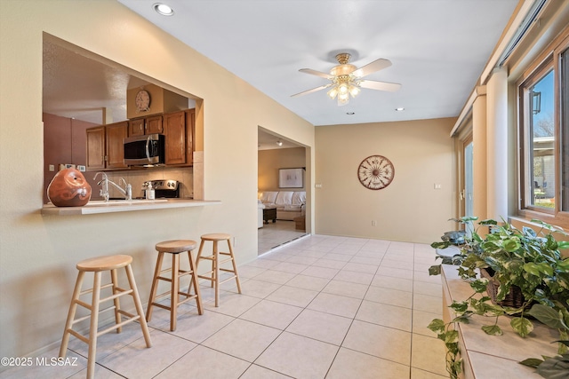 kitchen featuring light tile patterned flooring, tasteful backsplash, a kitchen bar, ceiling fan, and stainless steel appliances