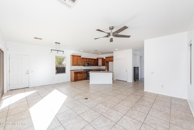 kitchen with light tile patterned floors, stainless steel appliances, decorative backsplash, a kitchen island with sink, and sink