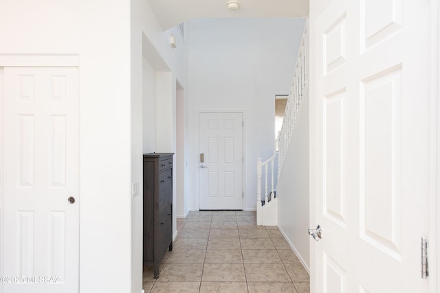 hallway featuring stairs, light tile patterned flooring, and baseboards