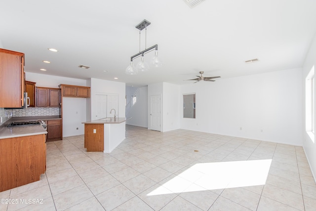 kitchen with visible vents, brown cabinets, a sink, backsplash, and open floor plan