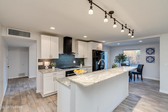 kitchen with light stone countertops, white microwave, light wood-type flooring, backsplash, and white cabinets