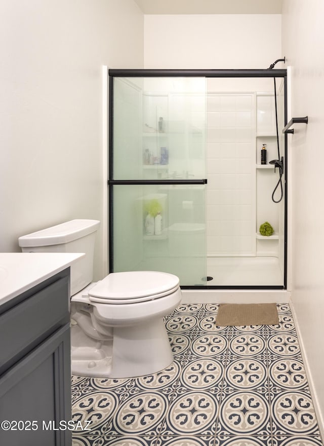 bathroom with a shower with door, vanity, tile patterned floors, and toilet