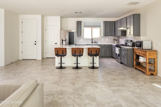 kitchen featuring a kitchen bar, tasteful backsplash, appliances with stainless steel finishes, gray cabinets, and a kitchen island