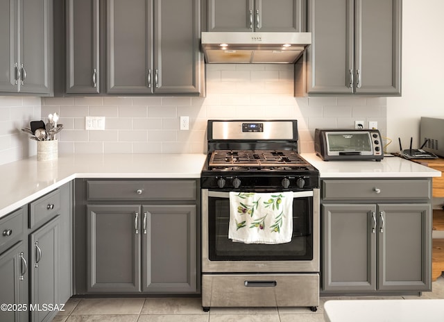 kitchen with light tile patterned flooring, gray cabinets, stainless steel gas range, and backsplash