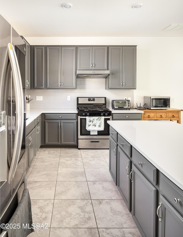 kitchen featuring backsplash, stainless steel appliances, light tile patterned floors, and gray cabinetry