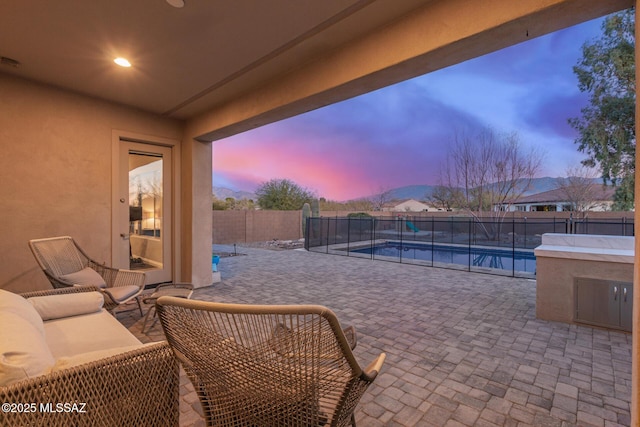 patio terrace at dusk featuring a fenced in pool and a mountain view