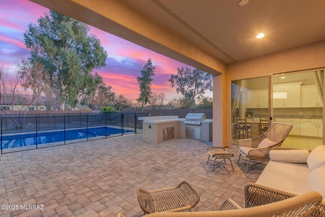 patio terrace at dusk featuring area for grilling, a fenced in pool, and an outdoor kitchen