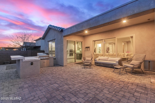 patio terrace at dusk featuring grilling area, outdoor lounge area, and an outdoor kitchen