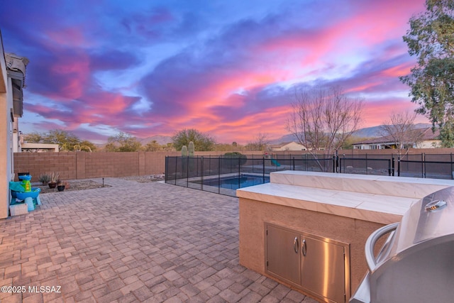 patio terrace at dusk with area for grilling and a fenced in pool