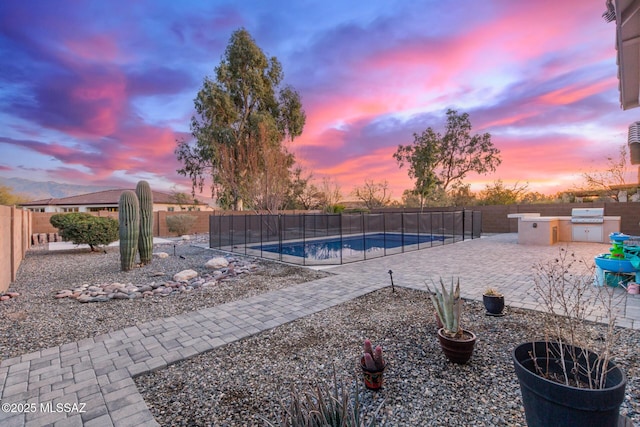 pool at dusk with exterior kitchen and a patio area