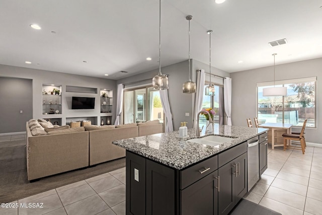 kitchen with light stone countertops, sink, a center island with sink, and decorative light fixtures