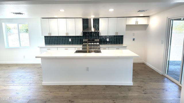 kitchen with stainless steel range with electric cooktop, white cabinetry, hardwood / wood-style flooring, a center island with sink, and wall chimney range hood