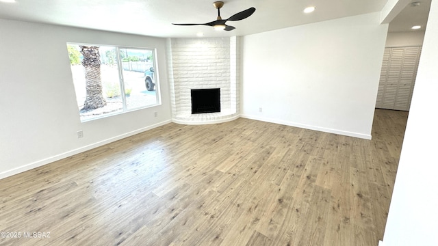 unfurnished living room featuring ceiling fan, light hardwood / wood-style floors, and a brick fireplace