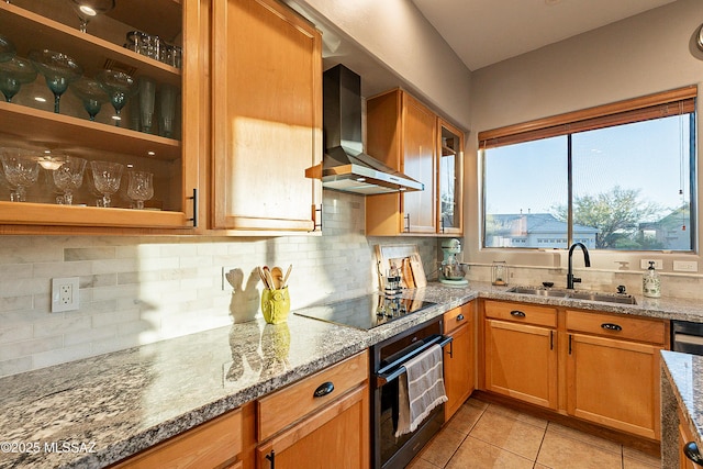 kitchen featuring wall chimney range hood, sink, light stone counters, black appliances, and decorative backsplash