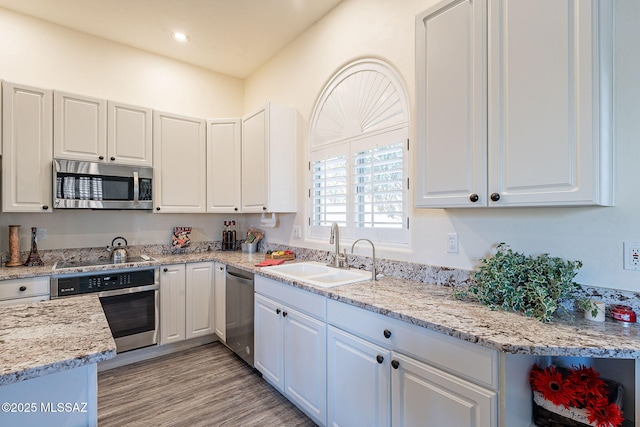 kitchen featuring light stone countertops, white cabinets, stainless steel appliances, sink, and light wood-type flooring