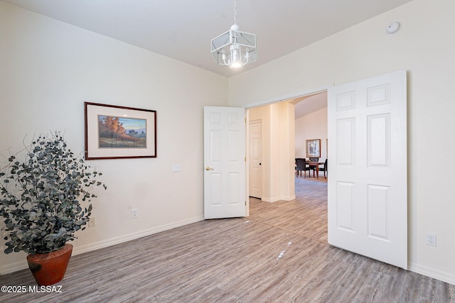 empty room featuring vaulted ceiling, an inviting chandelier, and hardwood / wood-style flooring