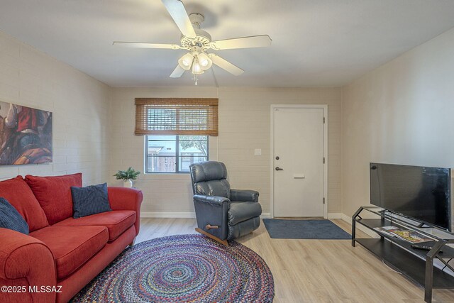 living room featuring ceiling fan, light wood-type flooring, and brick wall