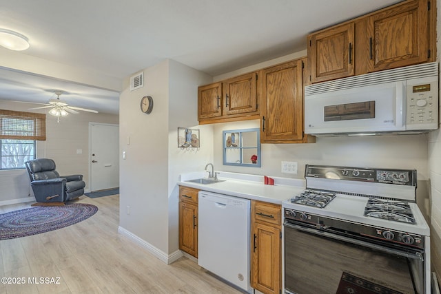 kitchen with a sink, visible vents, light countertops, light wood finished floors, and white appliances