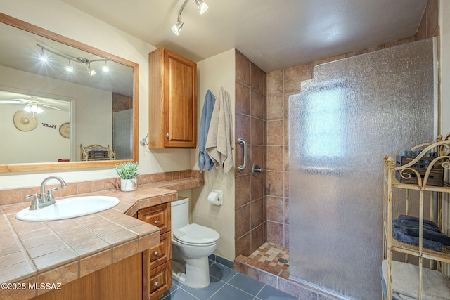 bathroom featuring tile patterned flooring, toilet, vanity, a ceiling fan, and tiled shower