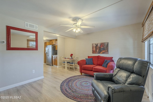 living room featuring a ceiling fan, visible vents, light wood-style floors, and baseboards